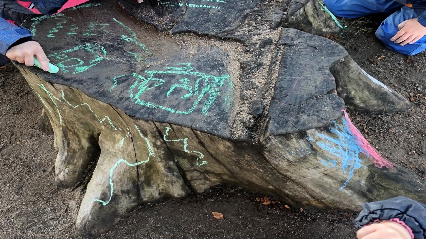 Barn ritar med krita på stubbe utomhus