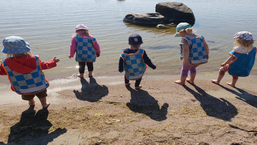 Barn doppar fötterna vid strandkanten